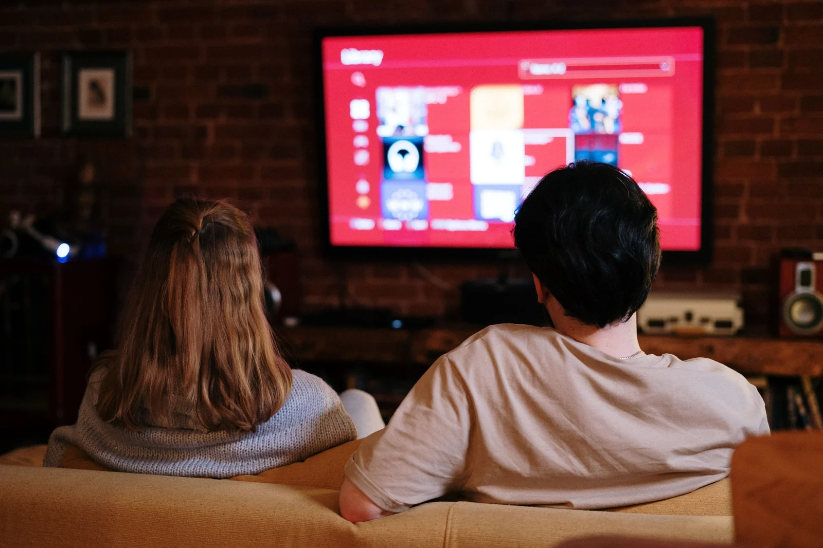 A couple seen from behind watching television together on a couch.